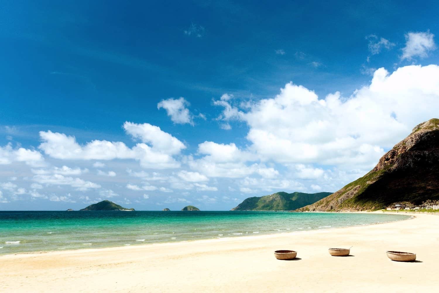 White sandy stretch of Dat Doc Beach with green hills in the background