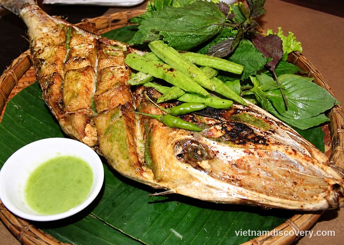 A grilled cá bò on a banana leaf with green chillies, herbs and a dipping sauce