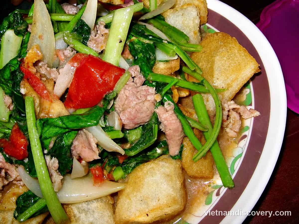 Fried phở pieces under beef, greens, onion and tomato