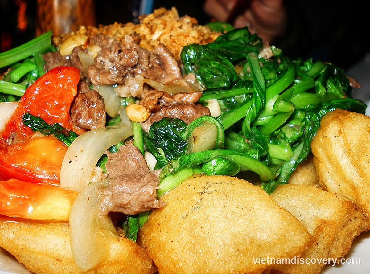 A plate of fried phở with beef, greens, tomato and fried shallots