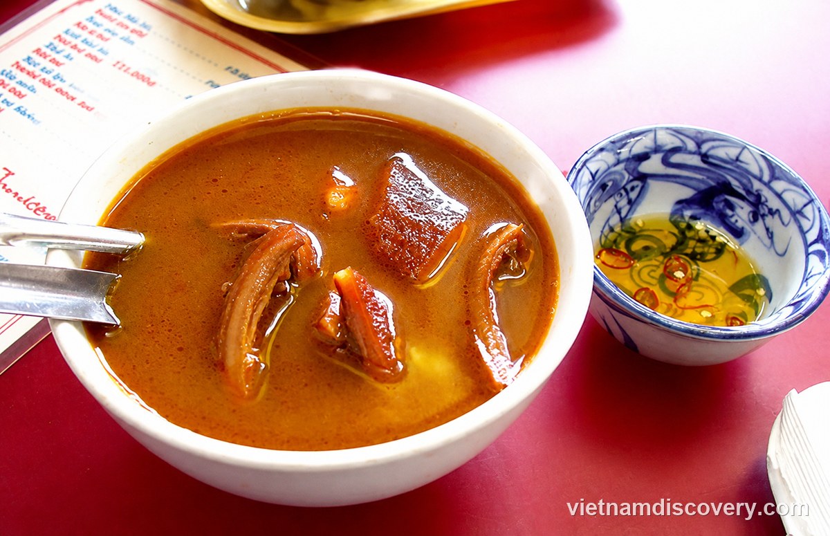 A bowl of phá lấu with a dish of chilli sauce