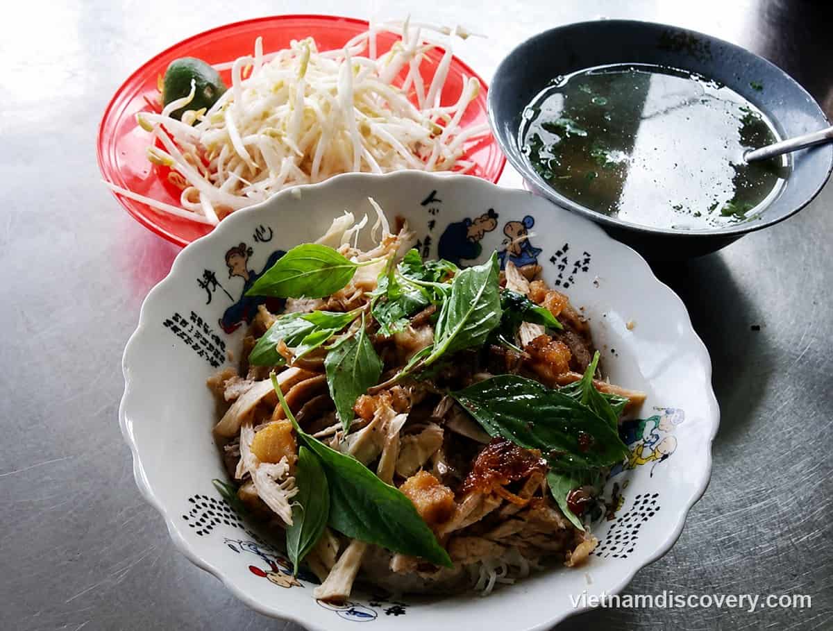 A bowl of dry phở topped with meat and herbs, with the broth served on the side