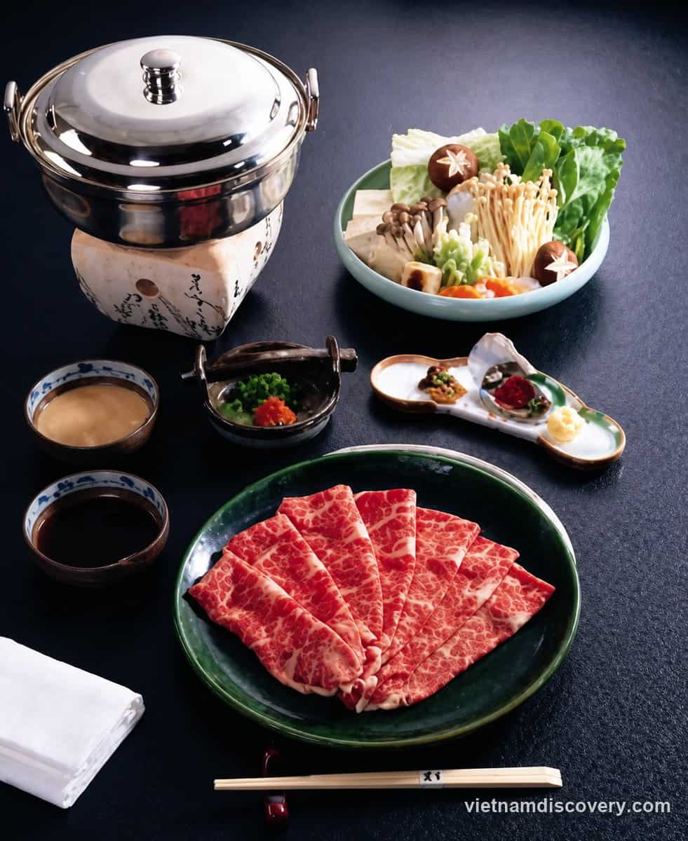 A hotpot set with a plate of thinly sliced beef, vegetables and dipping sauces